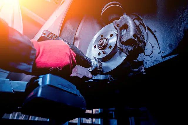 Technician inspecting and cleaning vehicle brake components during routine seasonal maintenance
