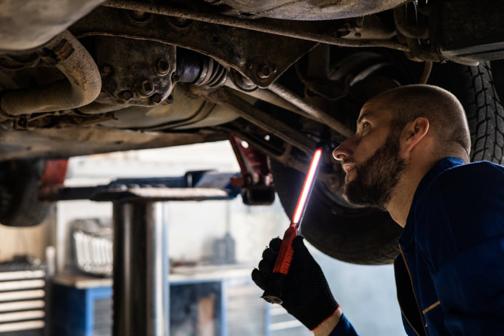 Mechanic using a work light to inspect the undercarriage of a vehicle on a lift after pothole damage