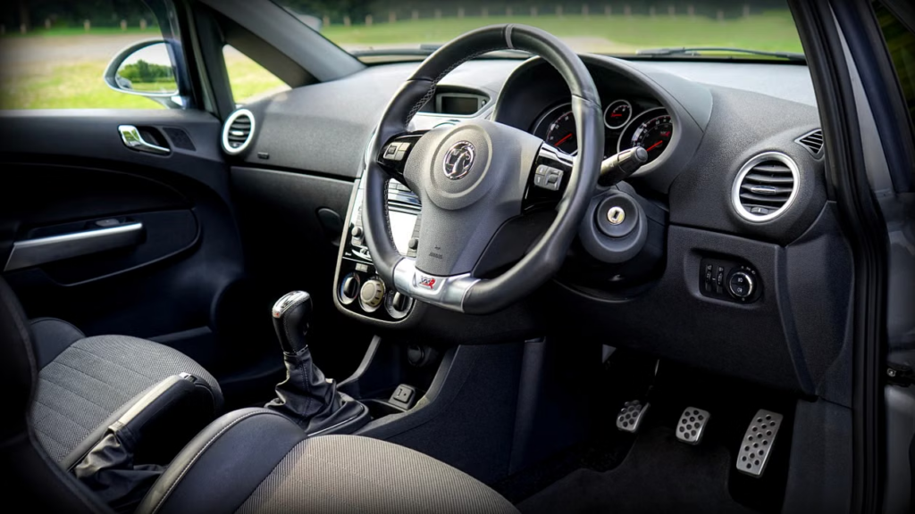 A car's interior showing the brake pedal, steering wheel, and dashboard gauges.