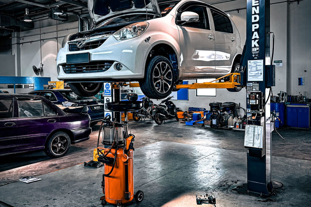 A car raised on a lift in a repair shop next to an oil drain unit.