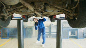 A mechanic inspecting underneath a raised vehicle.