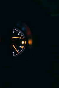 Vehicle dashboard showing a low fuel warning light and fuel gauge near empty during nighttime driving conditions