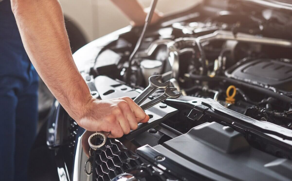 A mechanic holds two wrenches while working near an open car engine.