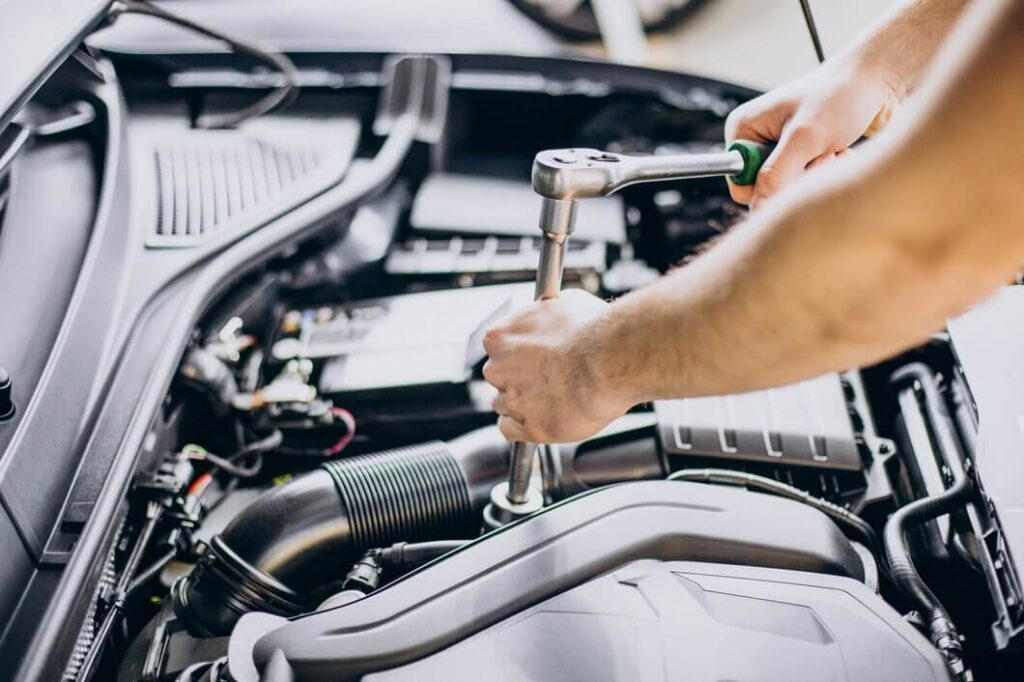 A mechanic uses a socket wrench on a component under the open hood.