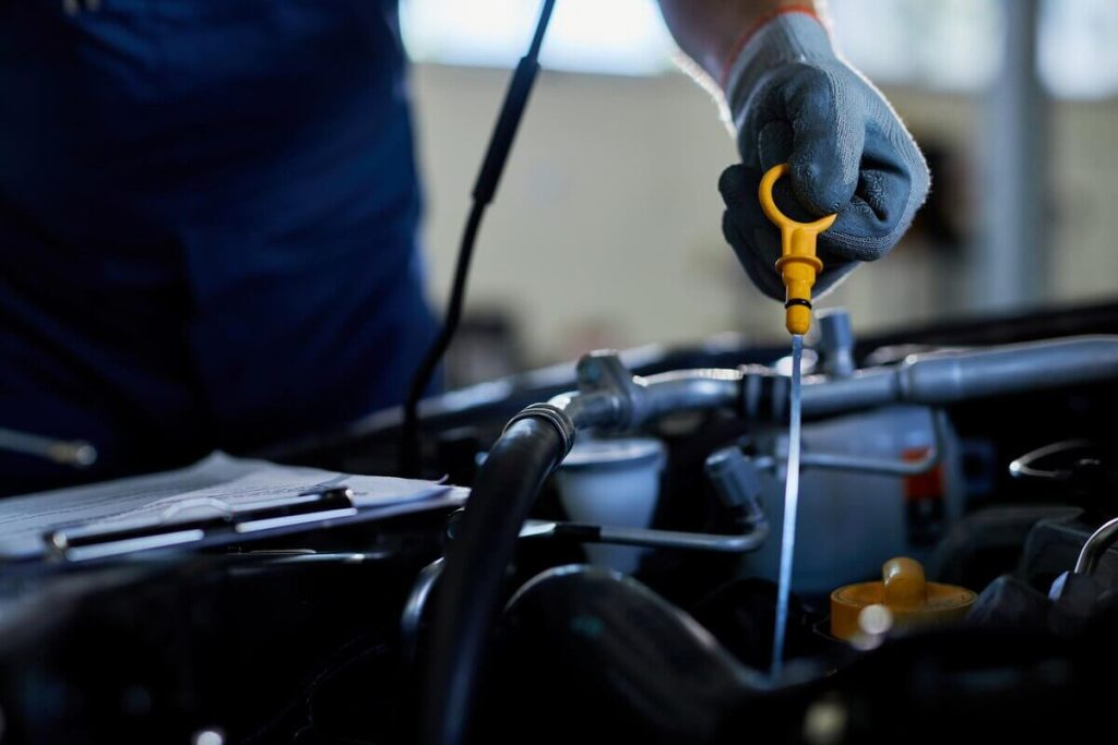 A gloved hand pulls an oil dipstick out of an engine for inspection.