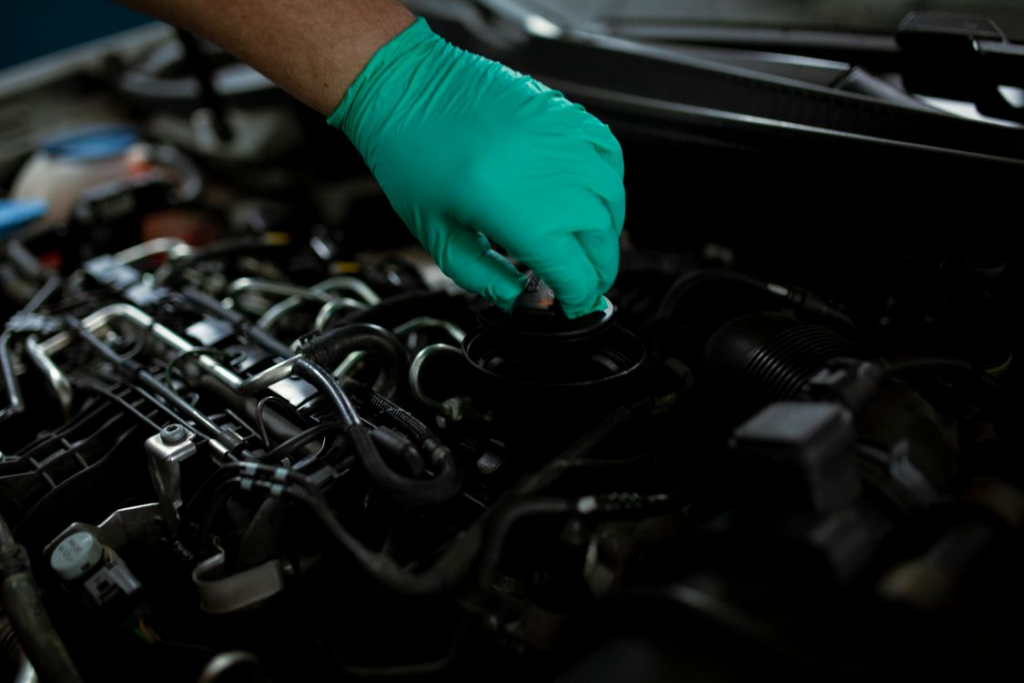 A gloved hand removing the oil filler cap on a car engine.
