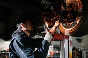 Mechanic inspecting brake components under a raised vehicle to diagnose a braking pull