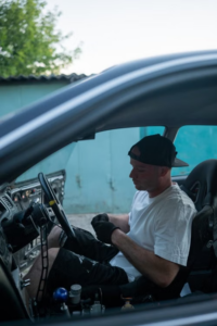 A mechanic inspecting a car steering wheel inside a vehicle to diagnose loose or hard steering causes.